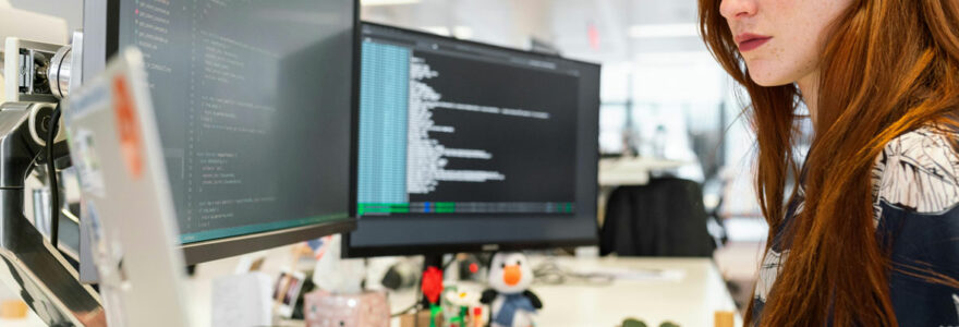 Femme développeuse programmant avec concentration sur deux moniteurs au bureau.