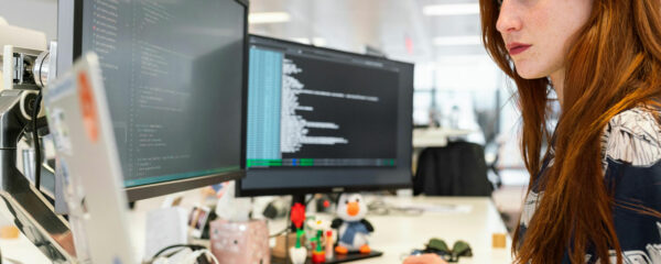 Femme développeuse programmant avec concentration sur deux moniteurs au bureau.